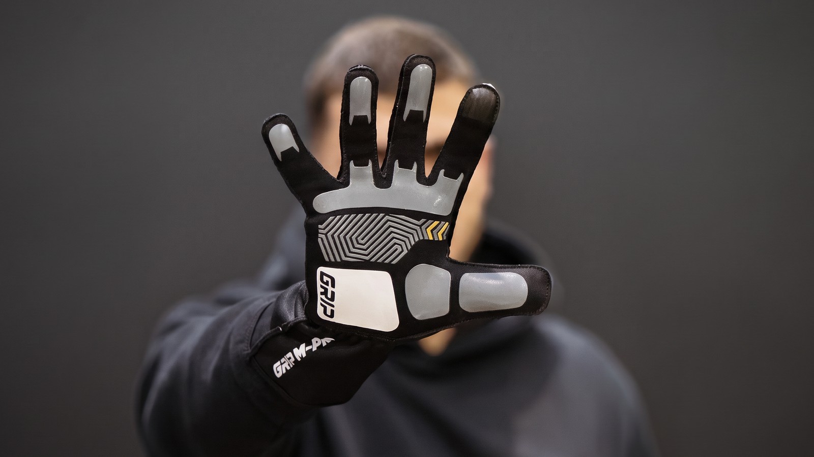 Syncmesh Grip M-PRO sim racing glove held palm-out, showing the silicone grip pattern across the palm and fingertips